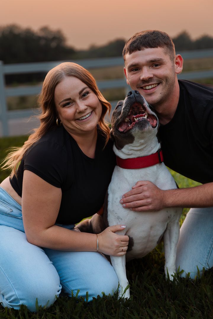 A couple and their white dog laying in grass during sunset enjoying a warm evening together.
