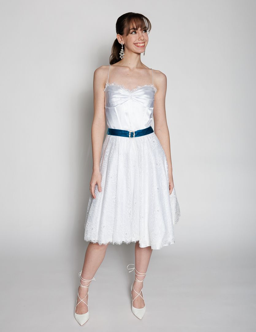 White strapless knee-length dress with tulle skirt and navy belt, paired with white lace-up heels.