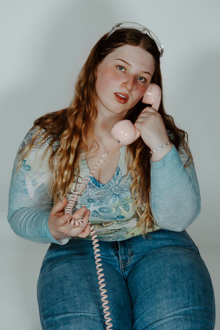 Creative self portrait series with retro telephone against light blue background wearing denim and paisley top.