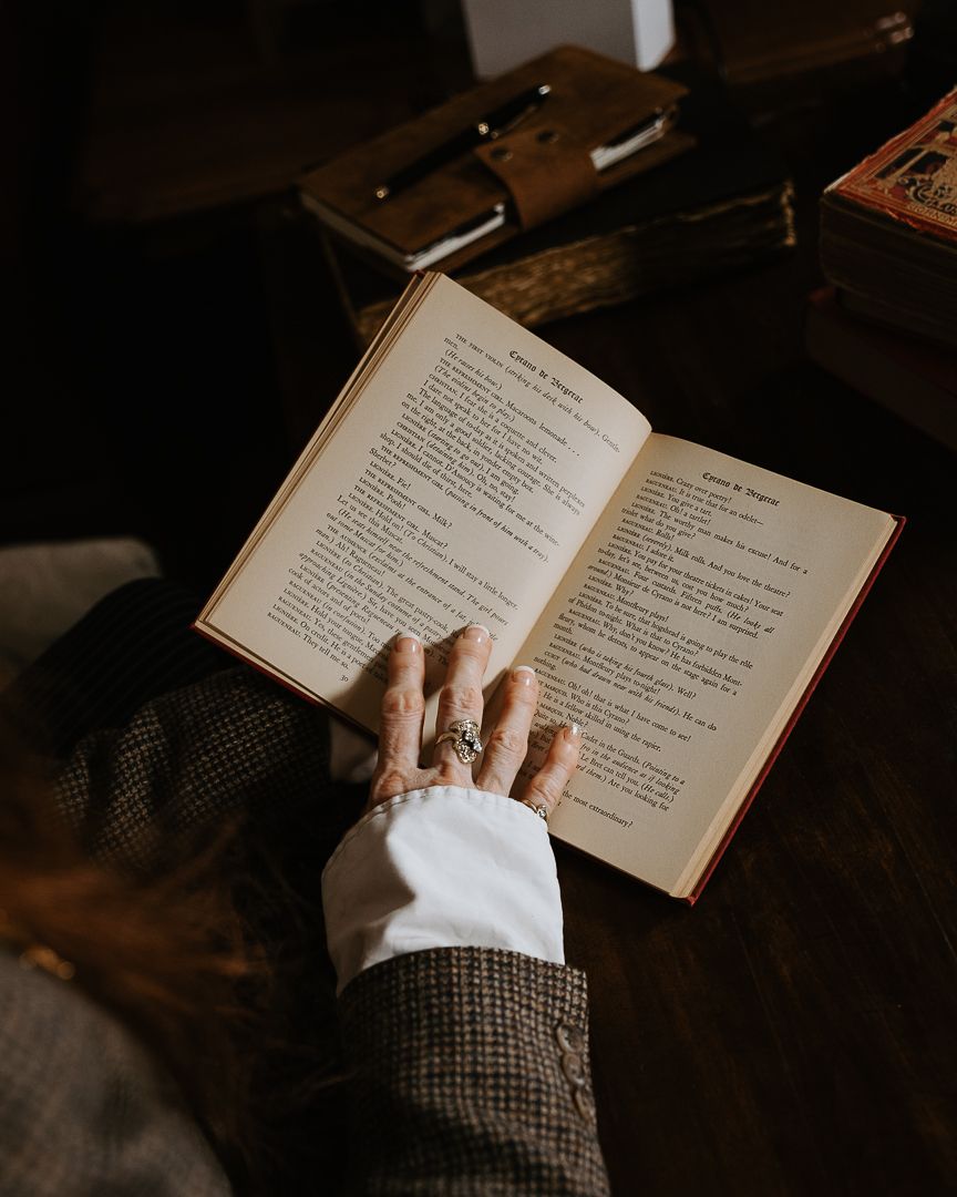 Hands gently hold an open vintage book against a dark wooden surface while reading its aged pages.