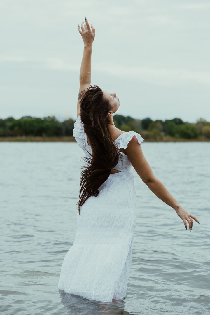 Woman in white dress spins joyfully in lake water with arms outstretched.