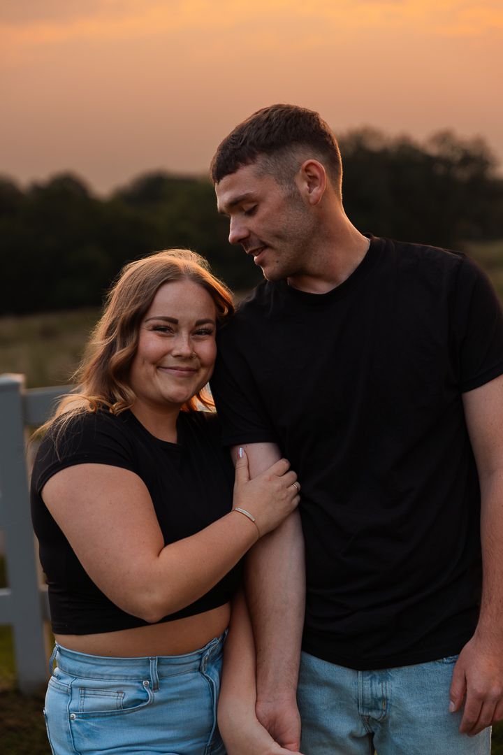 Couple in casual attire embracing during a warm sunset outdoors.