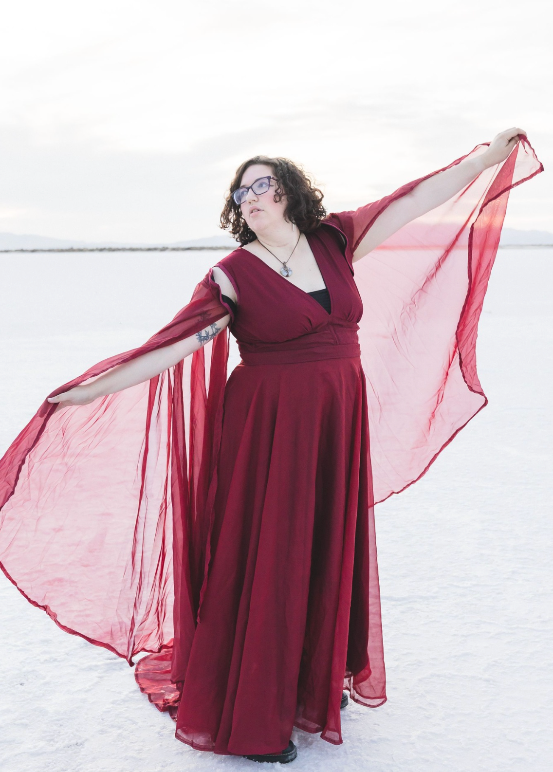 A person in a flowing burgundy dress poses gracefully against a snowy winter landscape.