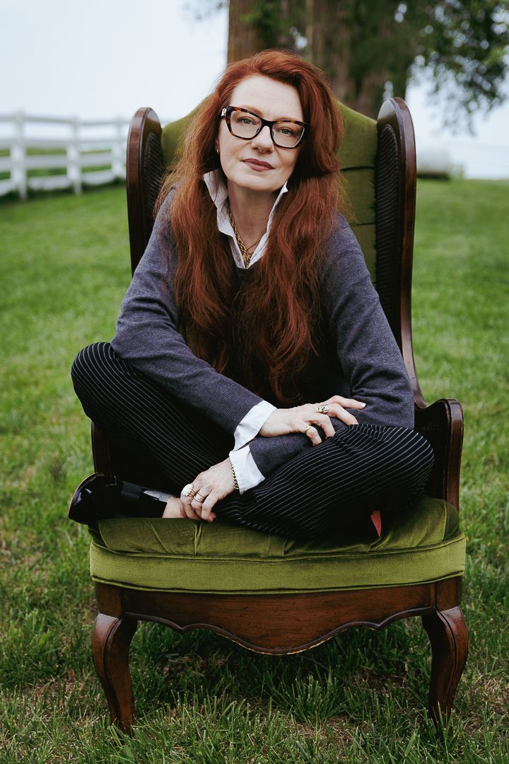 Person with red hair relaxes in a vintage olive green armchair on a grassy lawn.