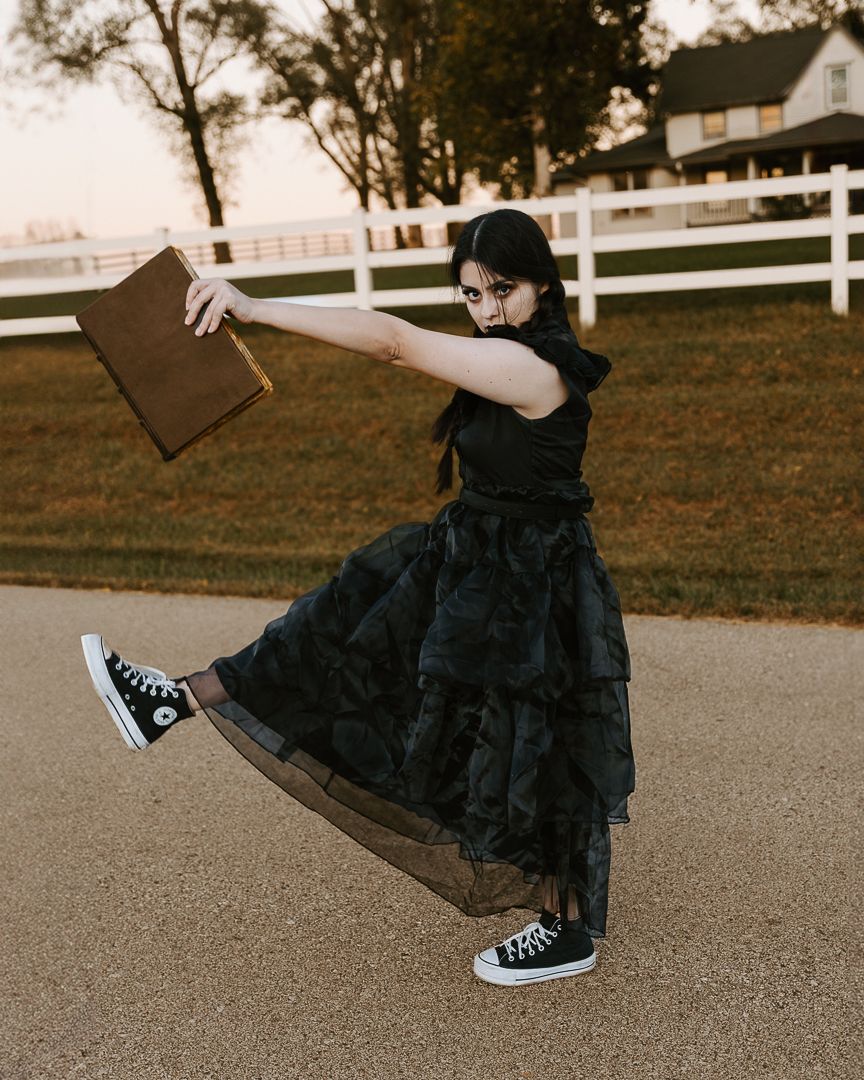 Person in black winter coat and sneakers performs playful jumping poses on a paved path near white fencing at sunset.