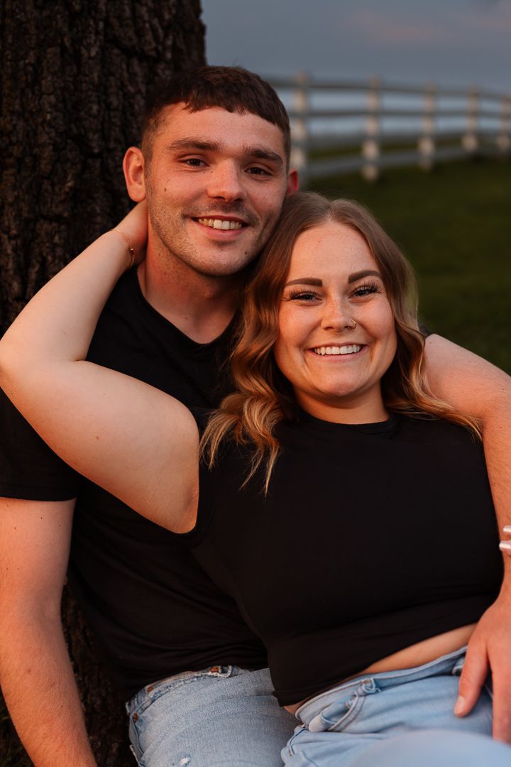 A couple sitting together outdoors during golden hour wearing matching black shirts and light jeans.
