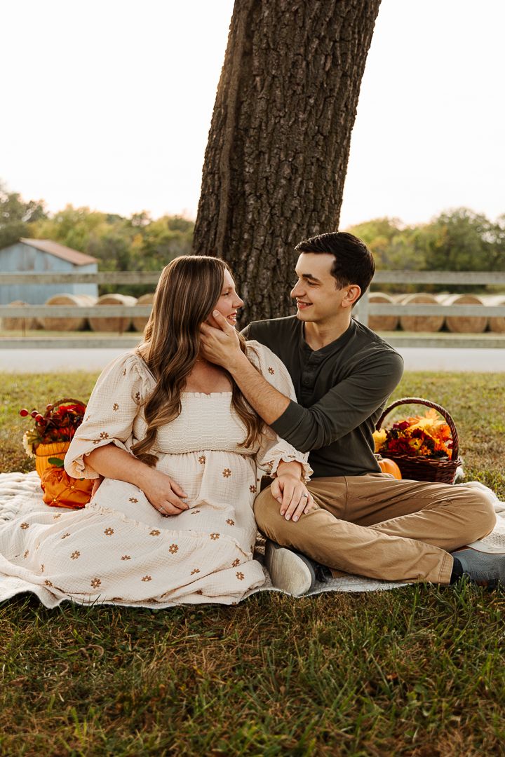 Couple lounging on grass during golden hour maternity session with orange floral decorations.
