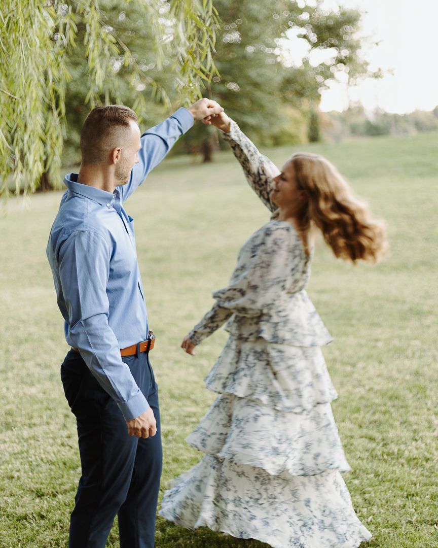 A couple spins and dances together on green grass in a romantic outdoor setting.