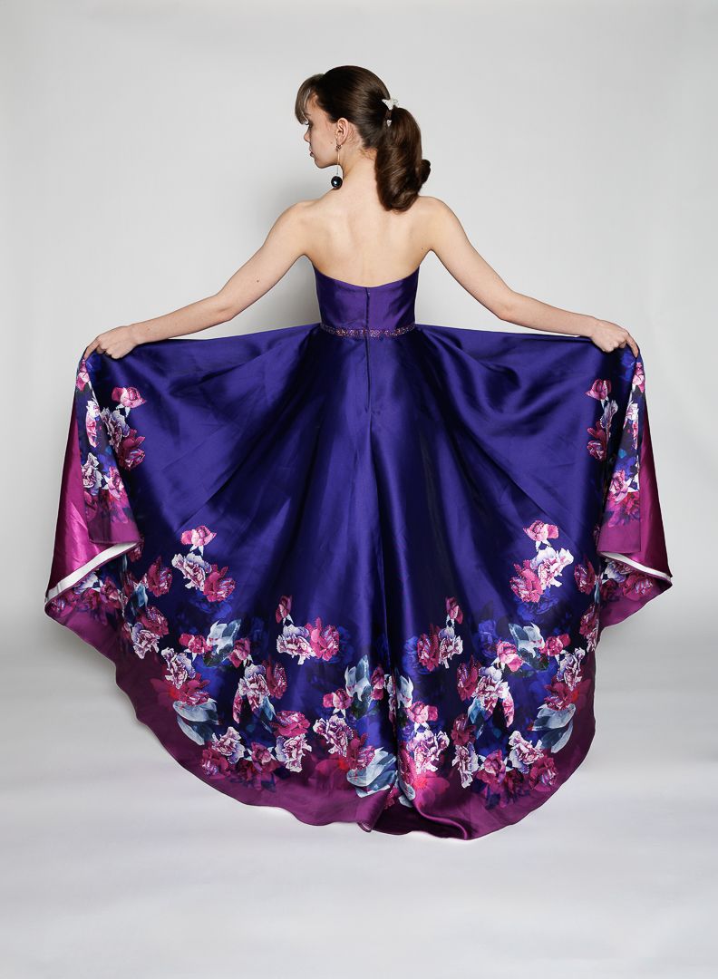Woman seen from behind in a strapless purple satin ball gown with a high-low hem and pink and blue floral print along the full skirt.