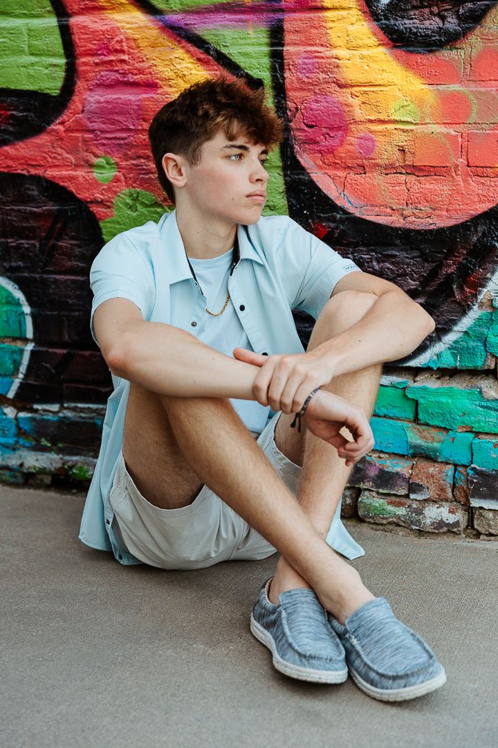 A casual portrait against a vibrant graffiti wall while wearing a light blue shirt and grey shoes.