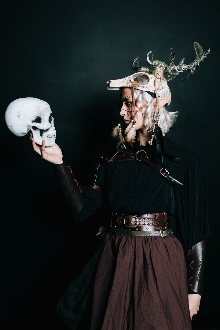 Dark fantasy costume featuring skull mask, antlers, and Victorian-style dress against black background.