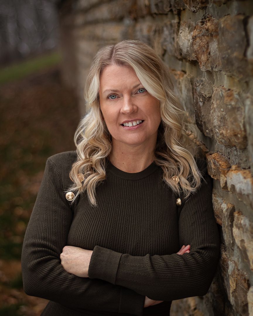 Woman in dark sweater poses against rustic stone wall outdoors.