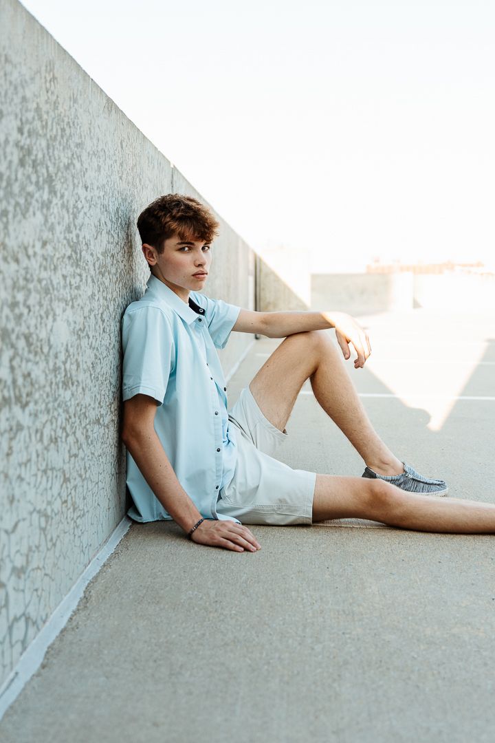 A casual summer fashion scene with someone reclining against a concrete wall in light blue attire.