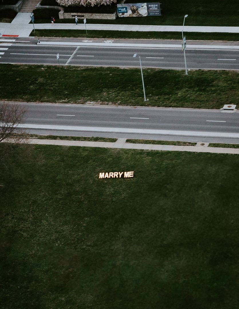 Text reading 'MARRY ME' written on grass next to a runway.