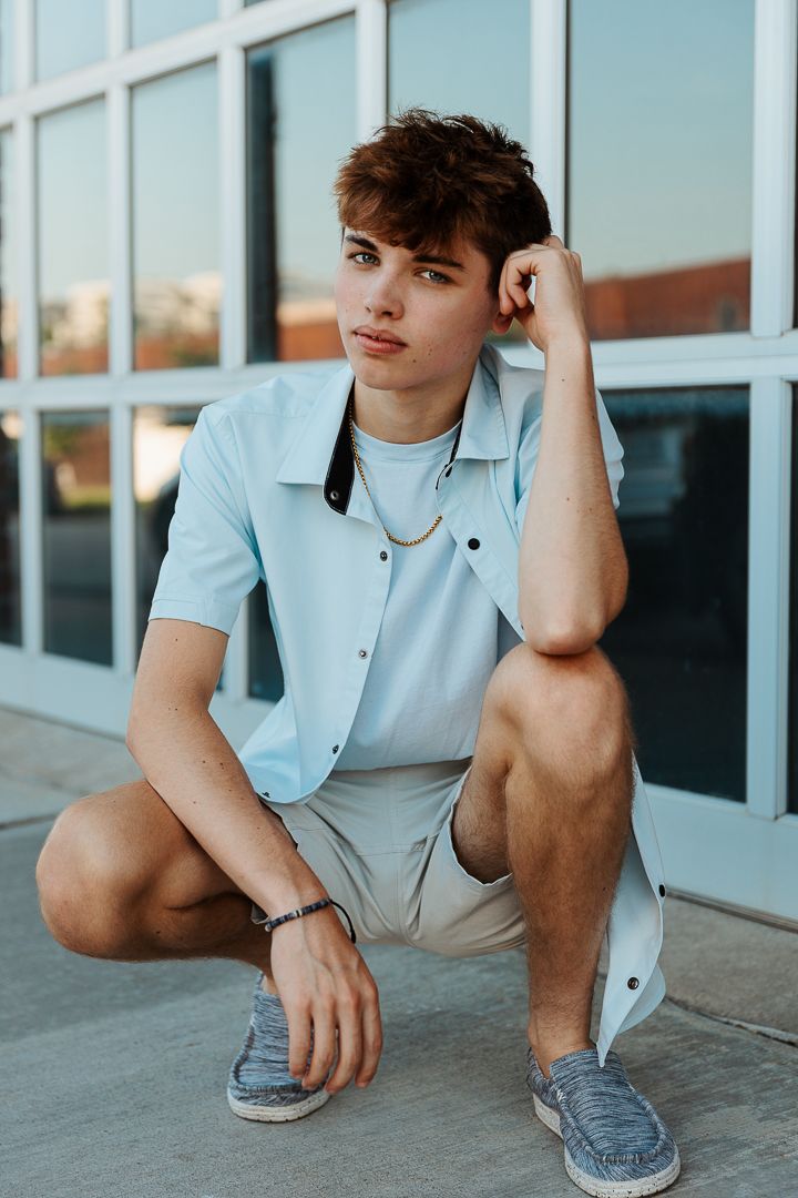 Casual summer fashion photo with light blue shirt and shorts against glass facade.
