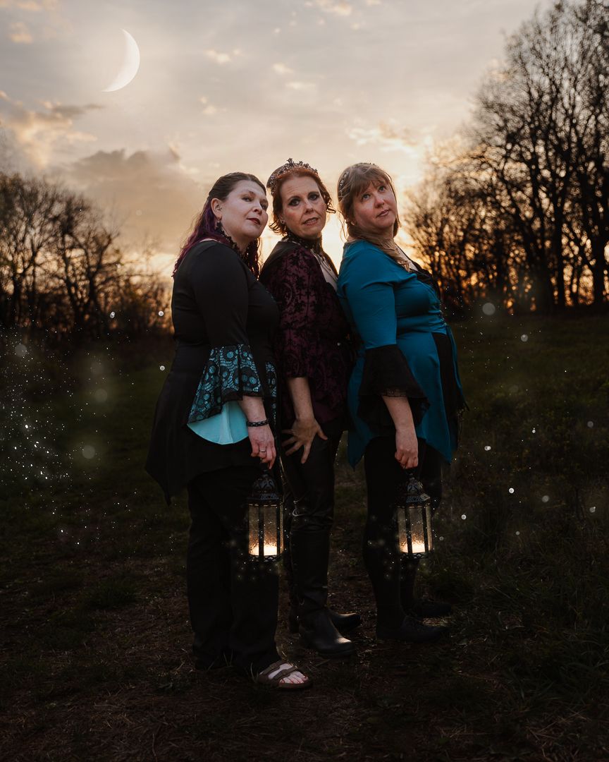 Three women holding lanterns stand back-to-back at dusk with a crescent moon and bare trees in the background.