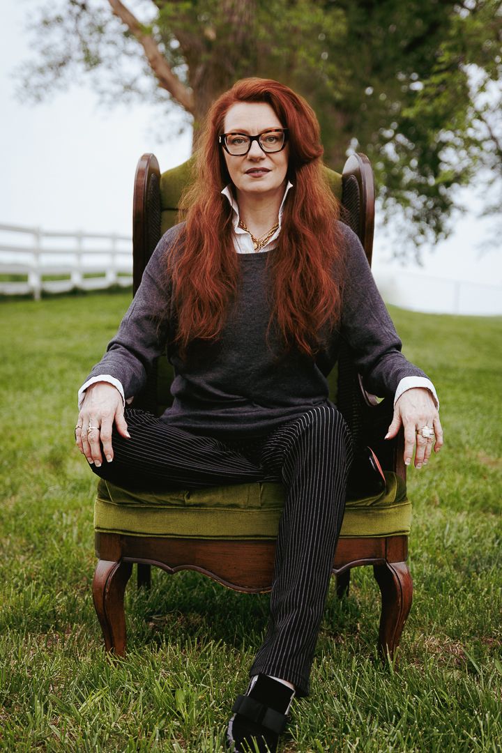 Casual portrait showing someone in striped pants and glasses lounging in an antique green chair on grass.