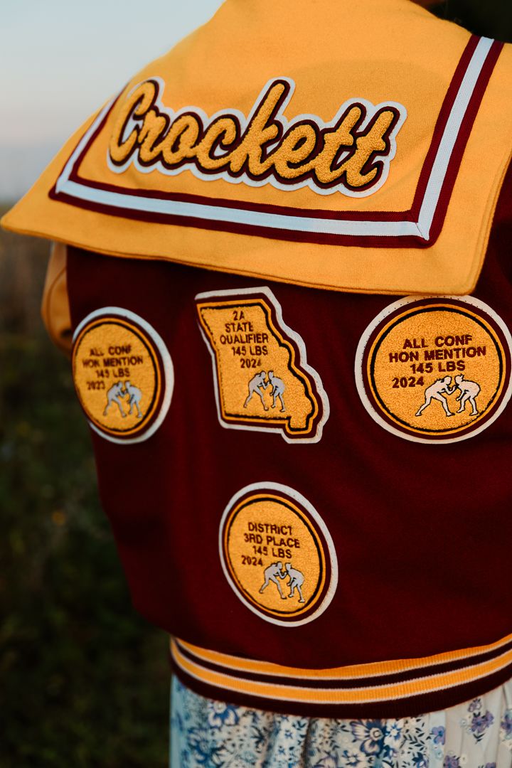 Close up details of maroon and gold letterman jacket patches and emblems.