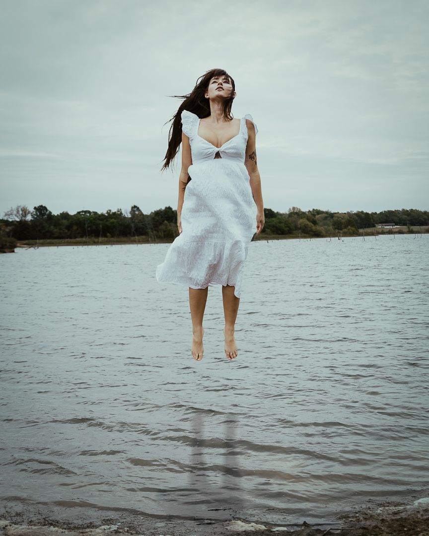 Woman in white dress creates ethereal scene standing in shallow water.