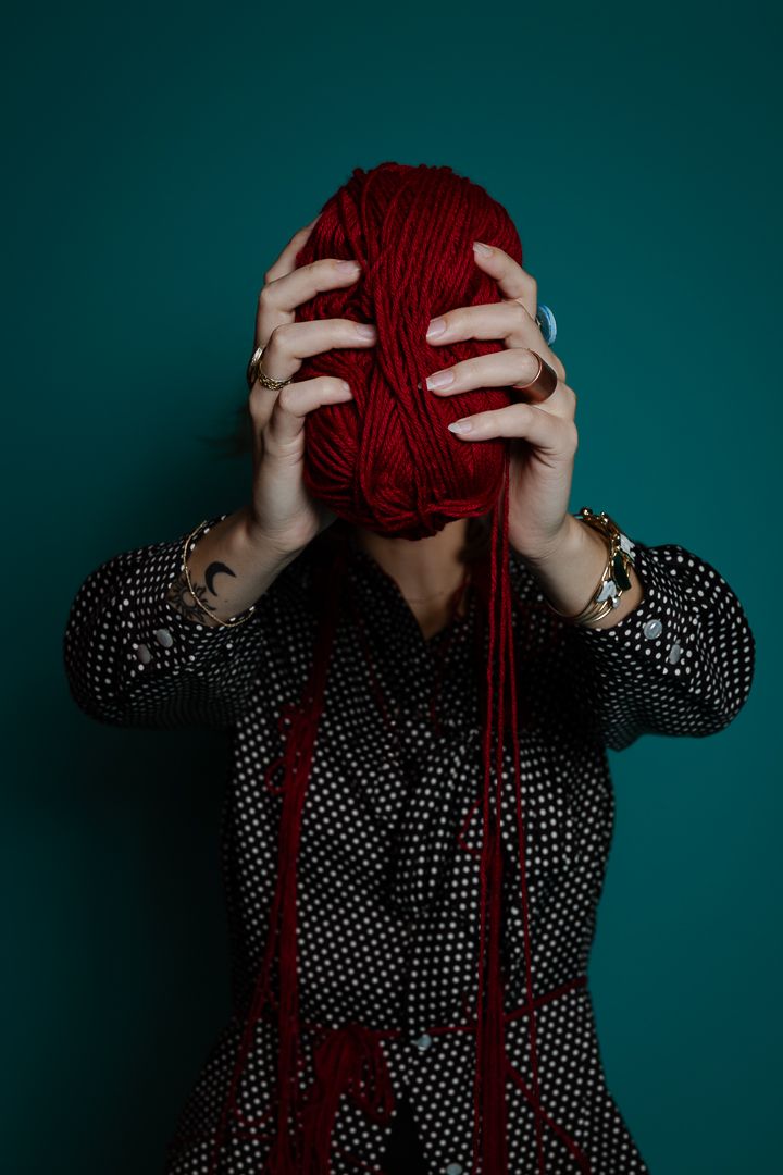 Fashion model in polka dot dress plays with red yarn against teal background in creative photo series.