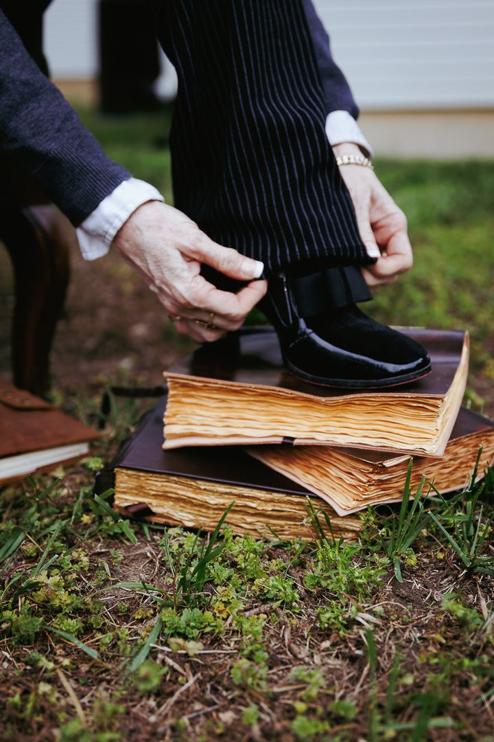 Hands holding and leafing through weathered pages of an old book placed on grass and soil.