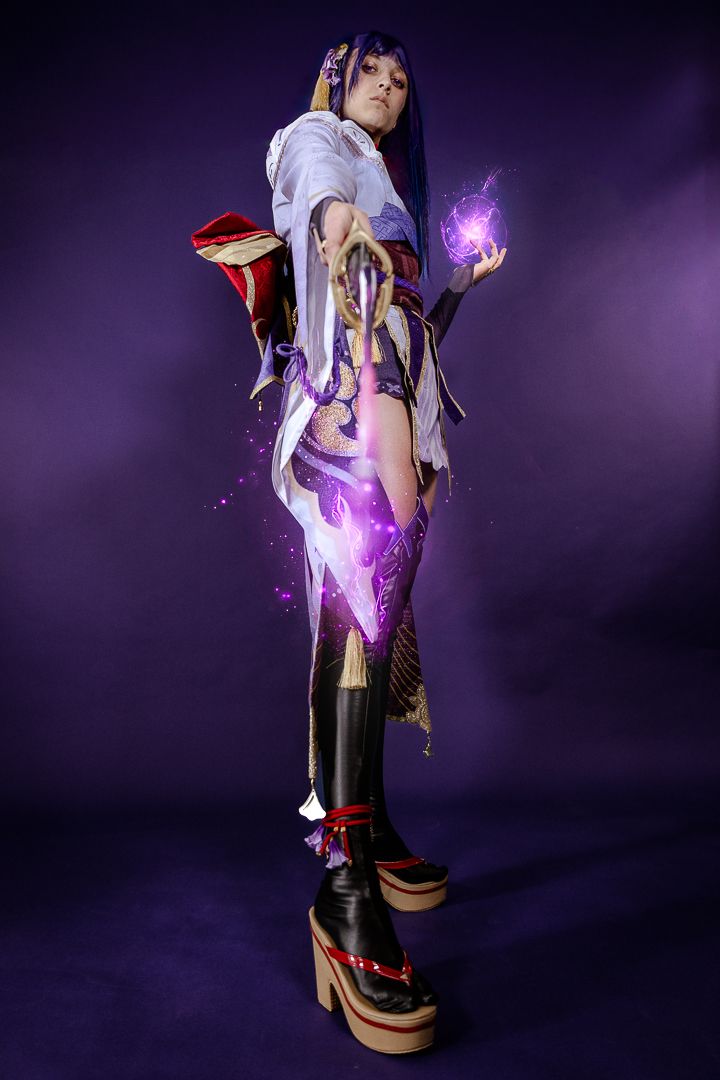 Cosplayer poses in fantasy anime-inspired outfit with glowing purple magical effects against dark background.