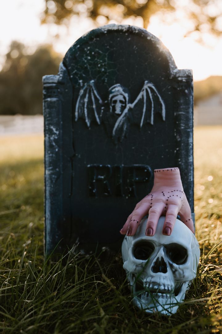 A series of decorative Halloween tombstones with skull designs arranged in grass during golden hour sunset lighting.