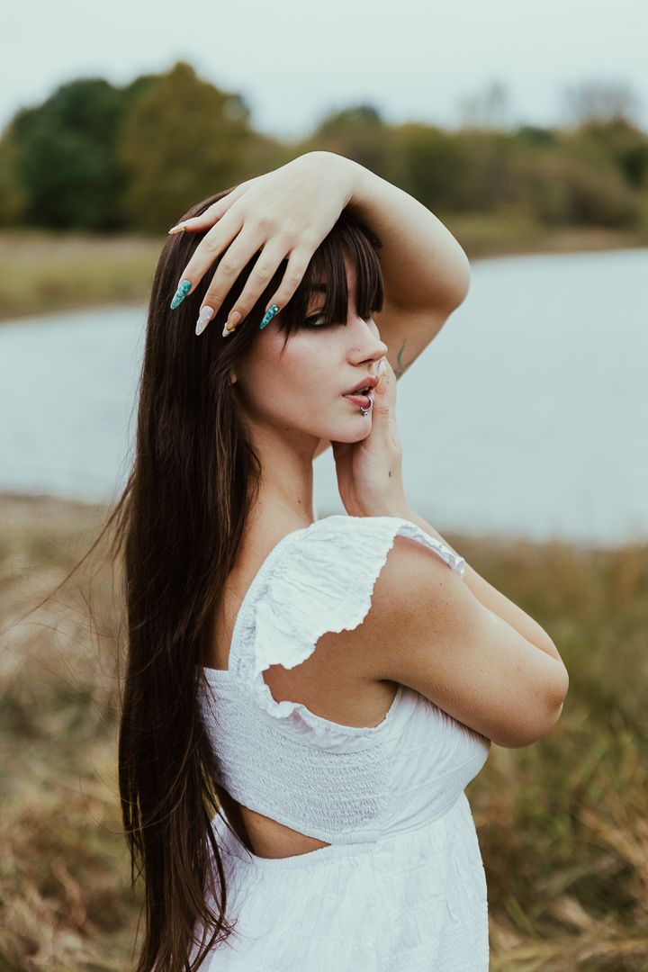 Artistic portrait of woman in white dress posing expressively by a lake.