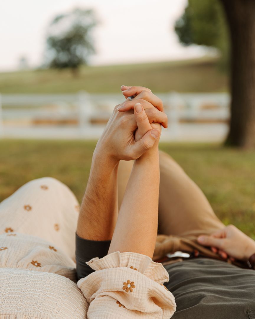 Two people's hands joined together while relaxing on a blanket outdoors in warm sunlight.