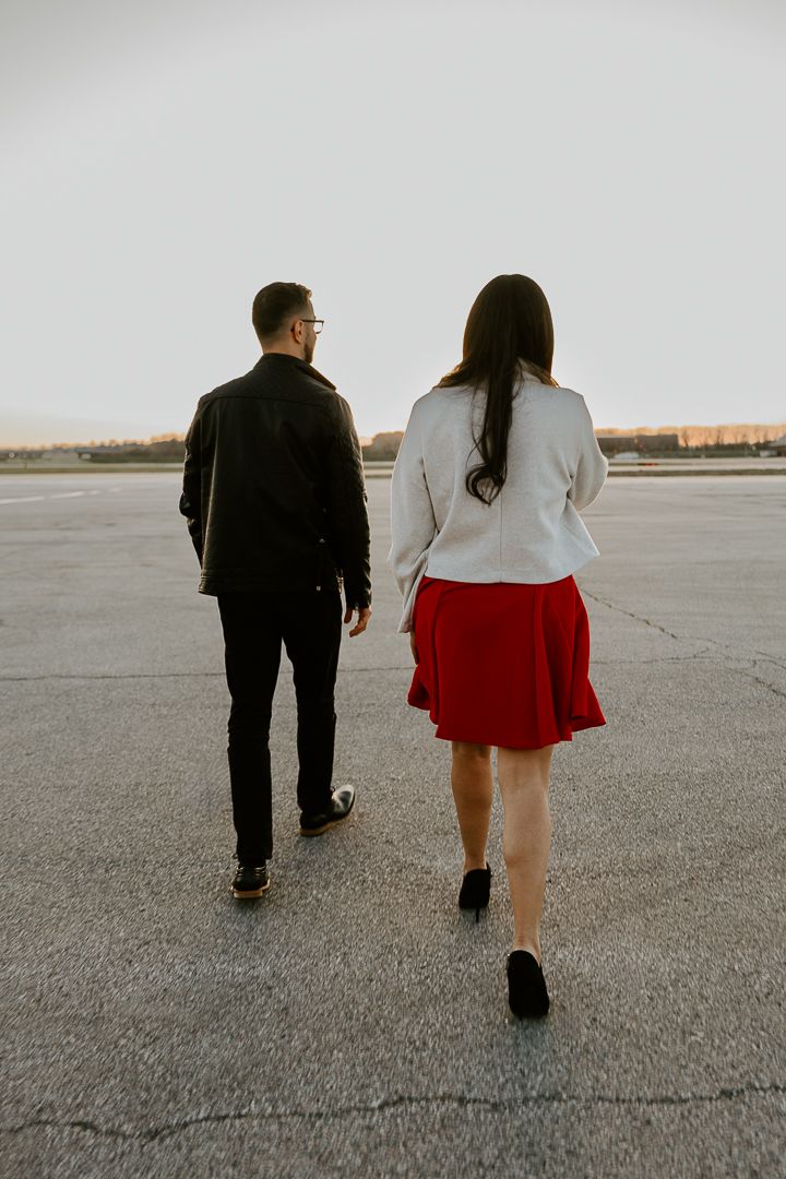 Couple walking together on an empty concrete surface in contrasting black and red outfits at sunset.