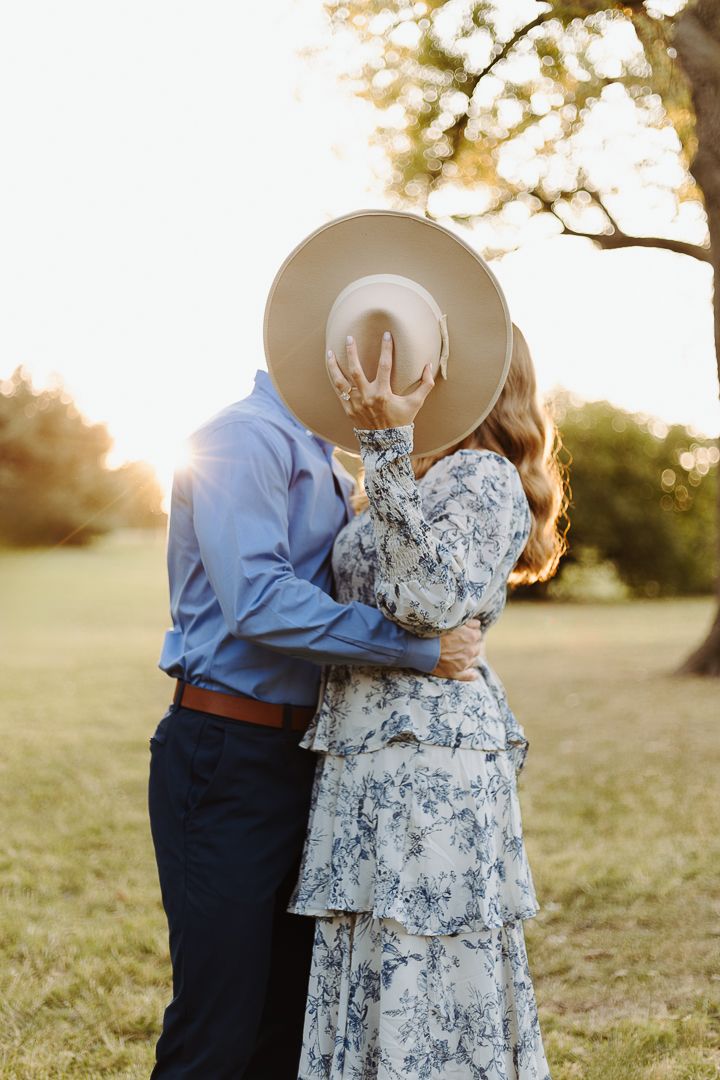 A romantic couple shares tender moments in a sunny field at golden hour, wearing blue shirt and floral dress.