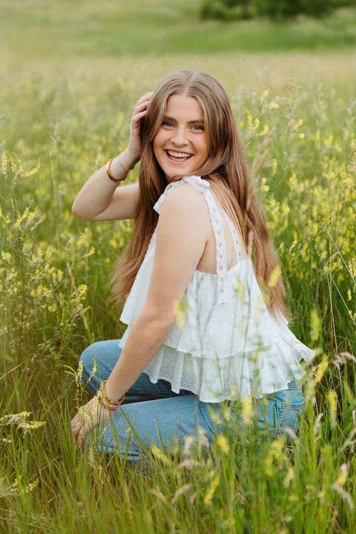 Person in white eyelet top and denim sits in tall grass during golden hour.