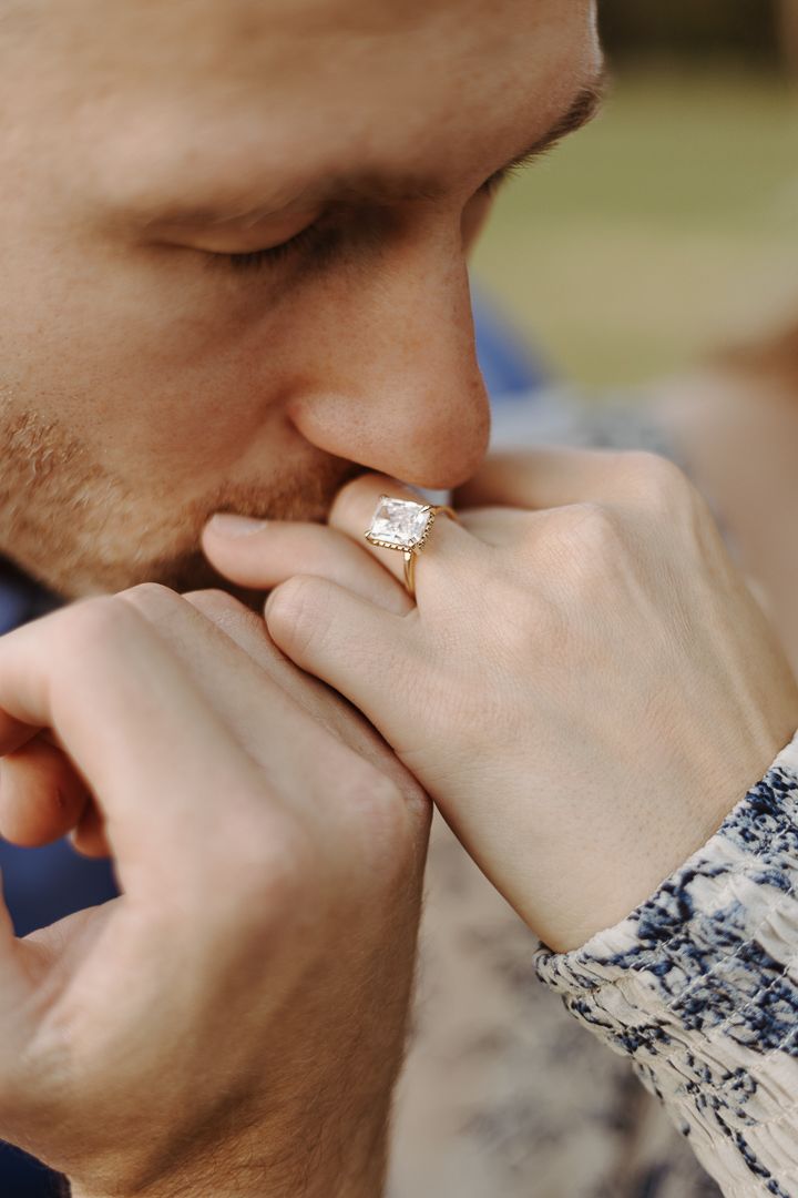 A tender moment as someone kisses a hand wearing a sparkling diamond engagement ring in an outdoor setting.