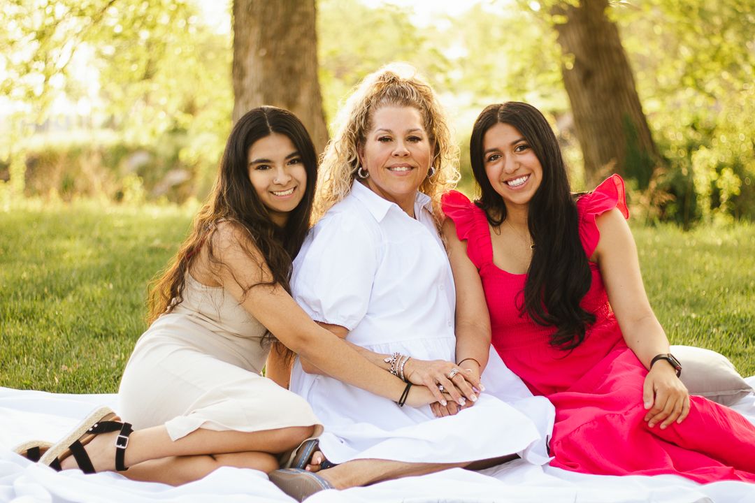 Family members wearing coordinated white and red outfits pose together outdoors in a sunny garden setting.