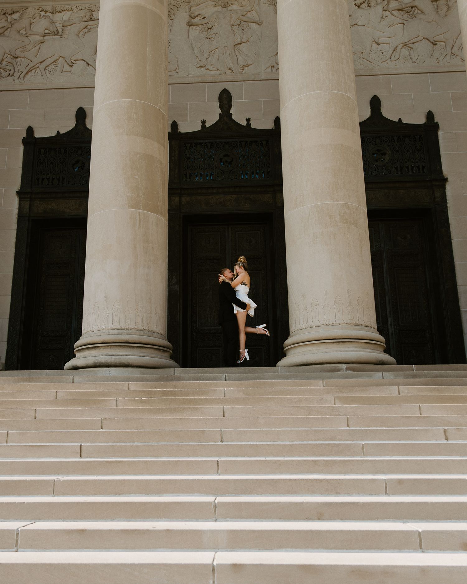 Couple embracing on grand neoclassical building steps with tall columns, romantic engagement photo.