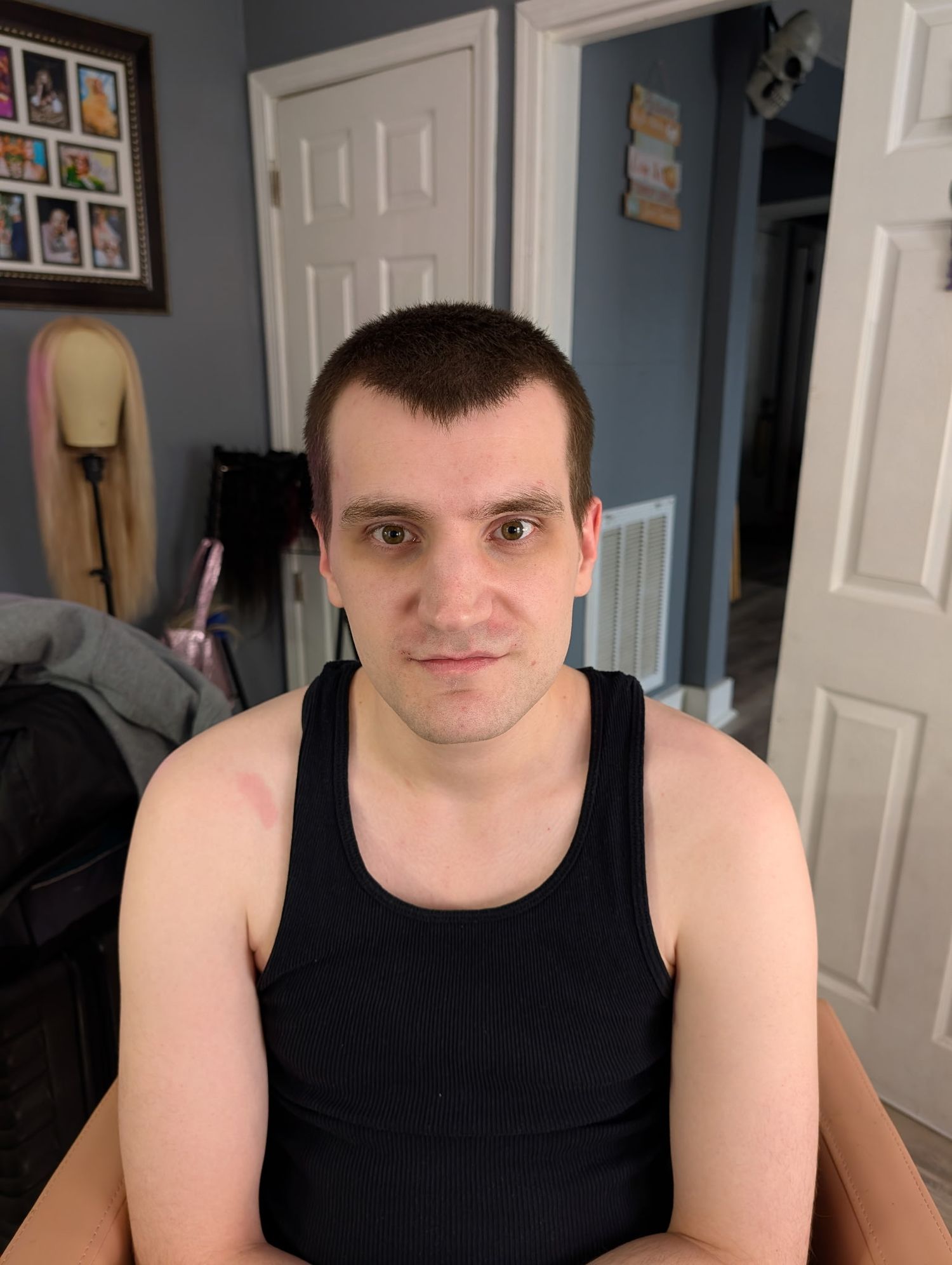Young man with short dark hair wearing a black tank top sits indoors near a white door.