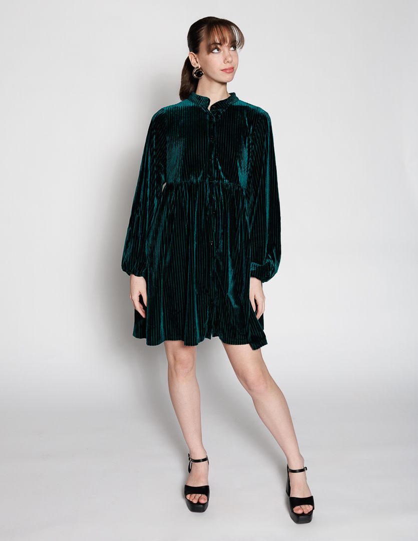 Woman wearing a teal green velvet mini dress with long sleeves, pleated skirt, and black platform heels.