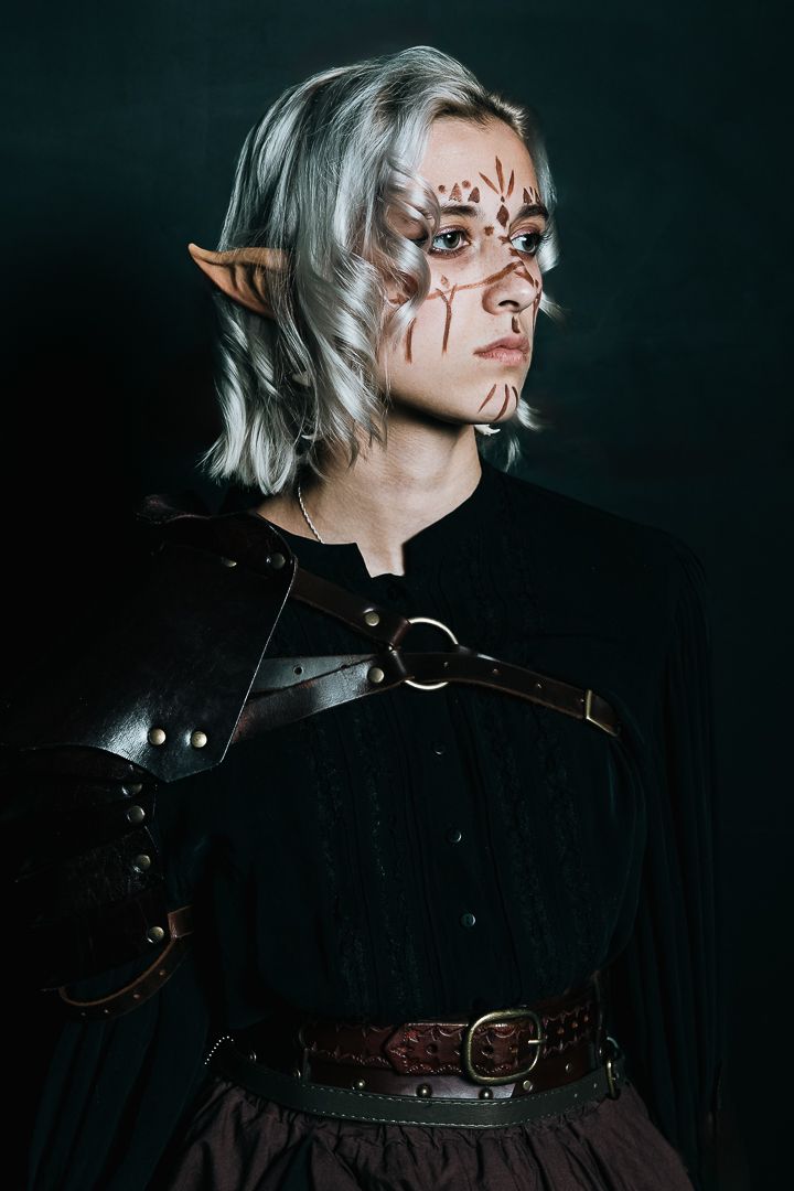 Dark artistic portrait with face paint and leather costume details.