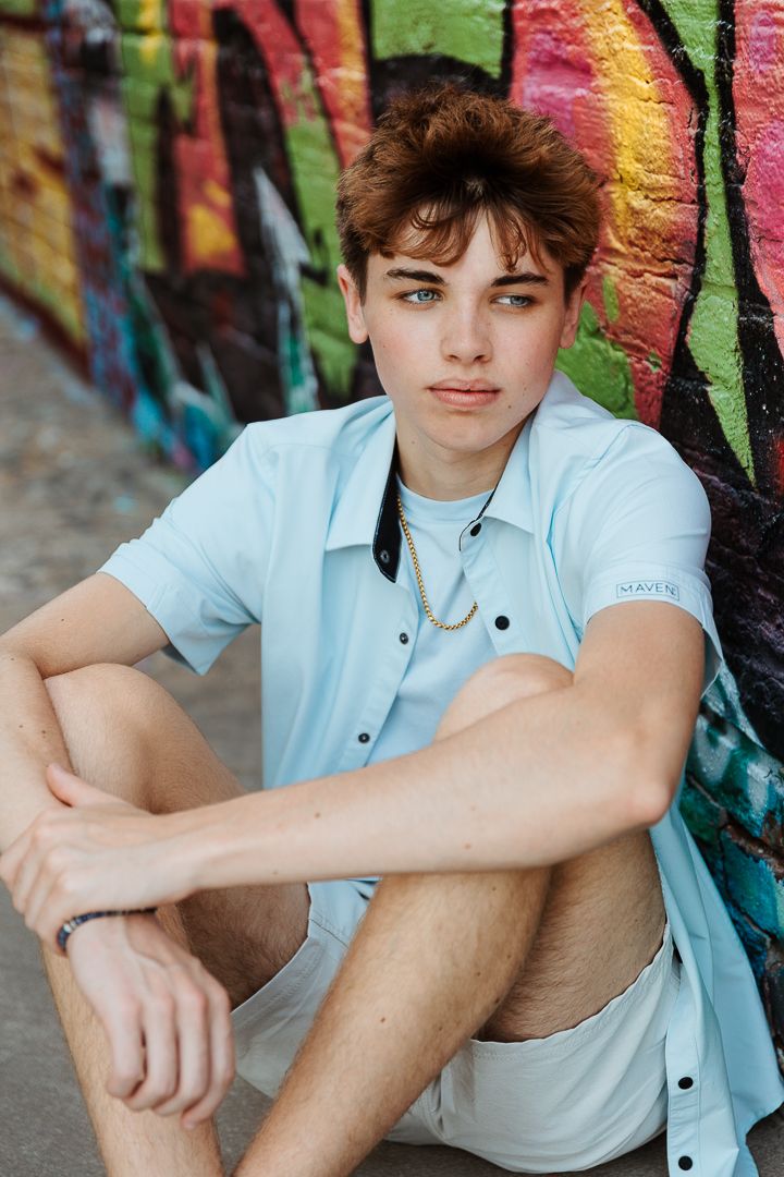 Person in casual blue shirt sitting against colorful graffiti wall during urban photoshoot.