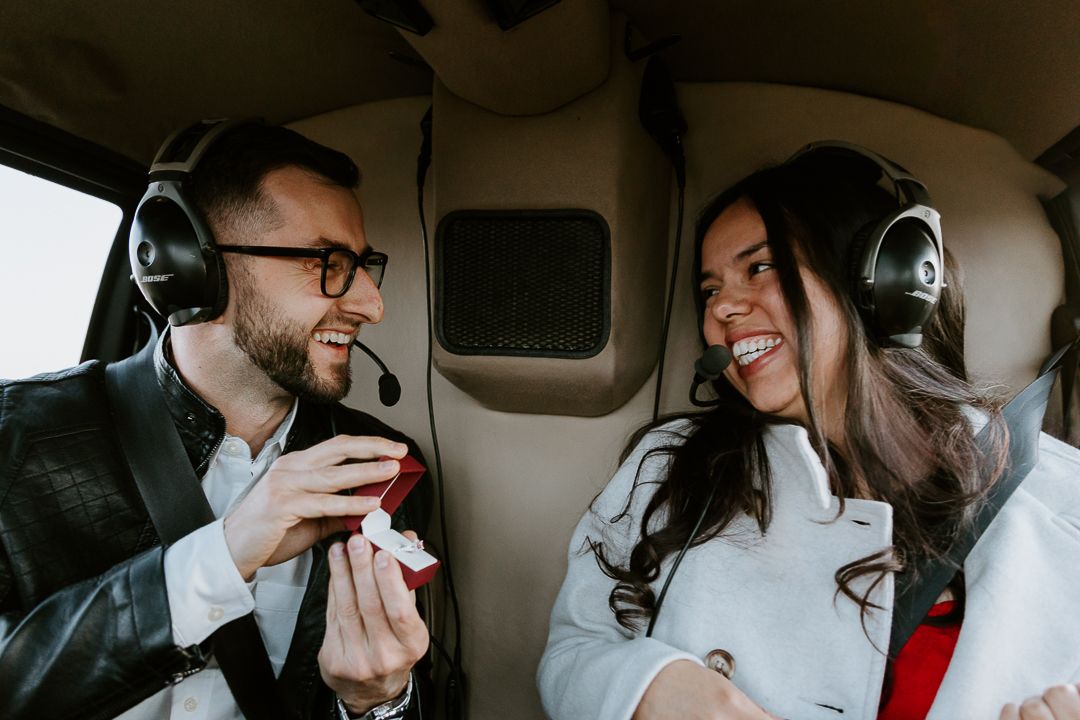 Two passengers wearing headphones share a joyful conversation while riding in the back of a vehicle.