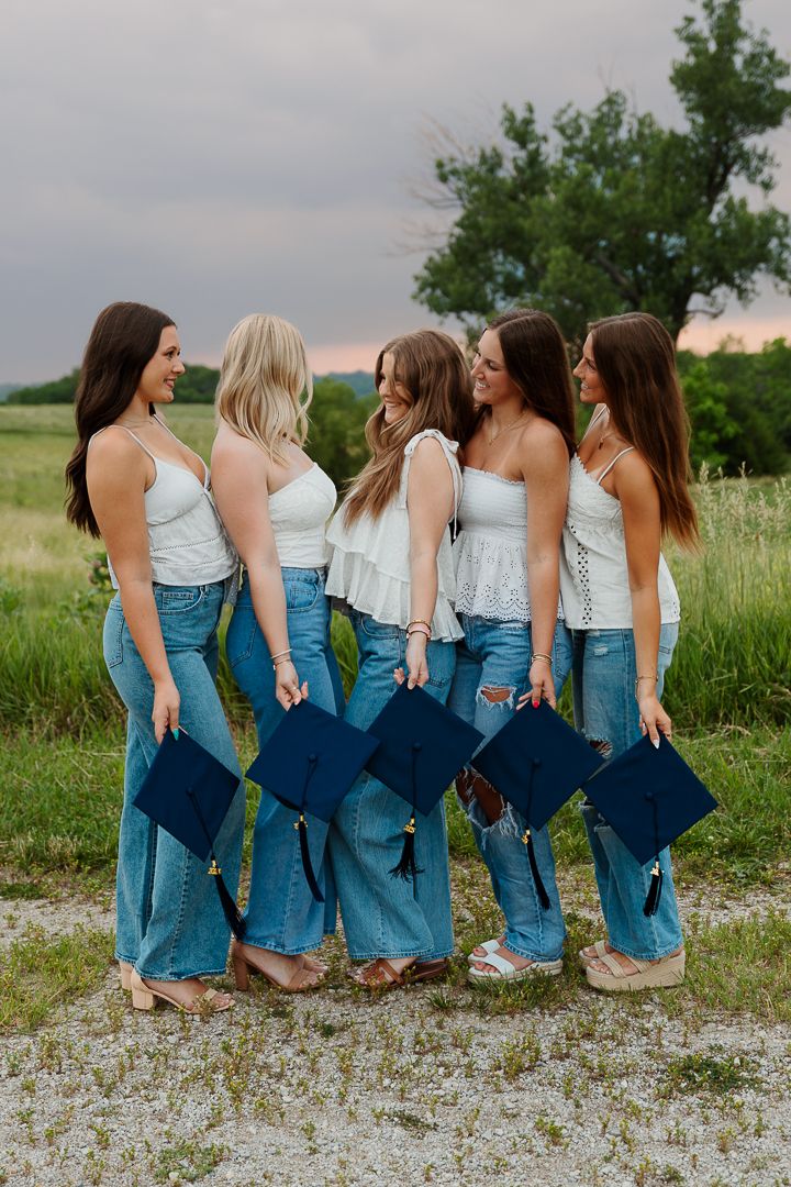 A group wearing matching white tops and jeans sits together in a grassy field at sunset.