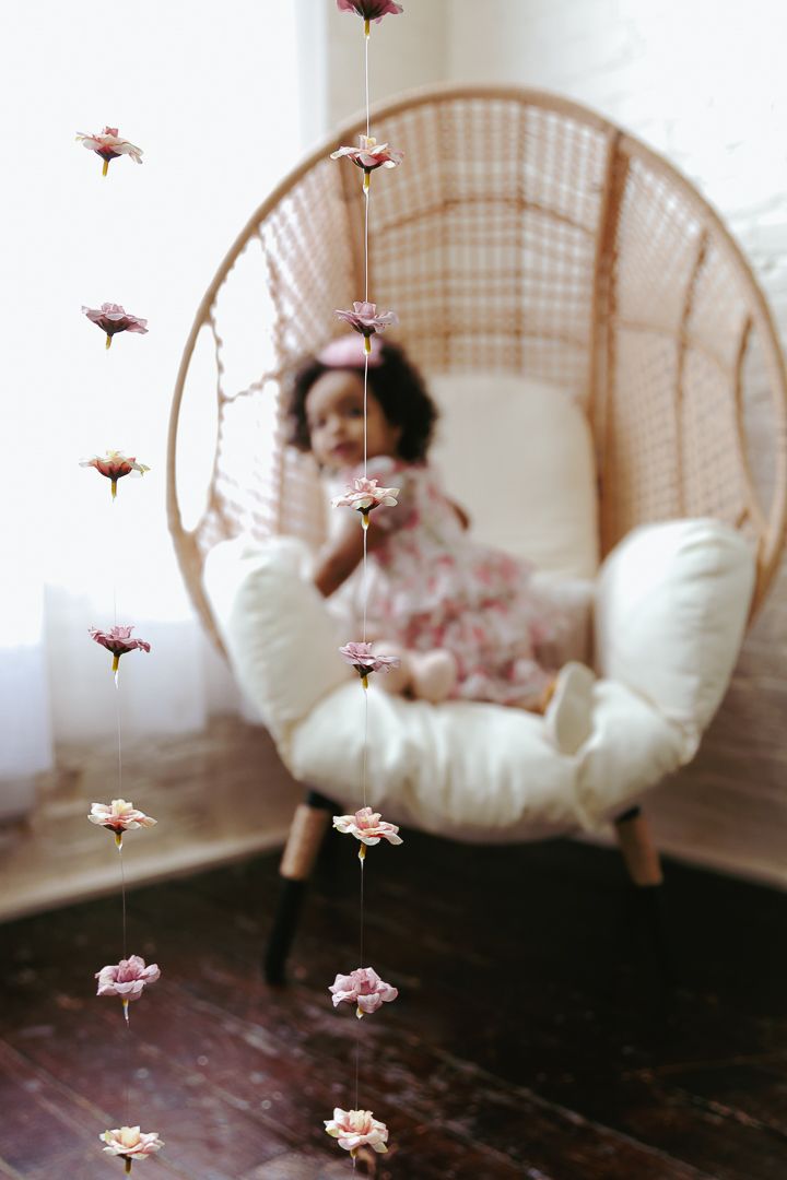 Dreamy pink flower petals float around a wicker peacock chair creating an ethereal atmosphere with soft lighting.