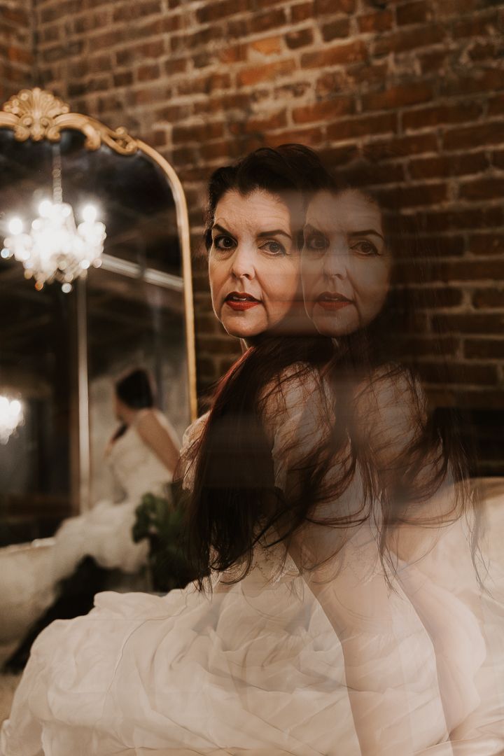 A dreamy double exposure portrait showing overlapping ethereal silhouettes against a dark brick wall background.