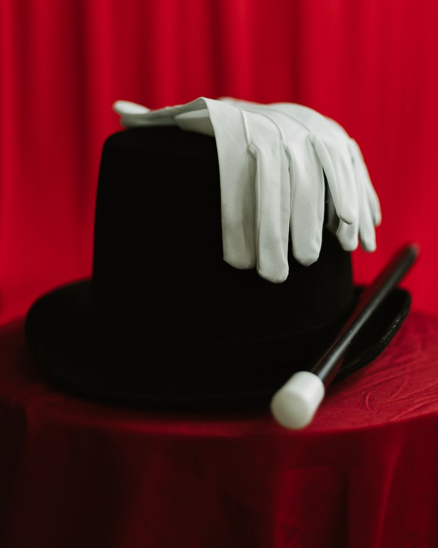 Black top hat with white gloves and magic wand on red velvet table, classic magician props for stage performance.