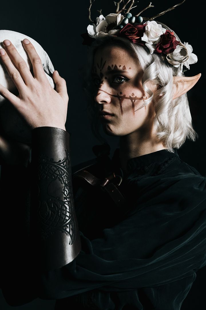 Dark fantasy character holding crystal skull wearing flowers and ethereal gothic costume.