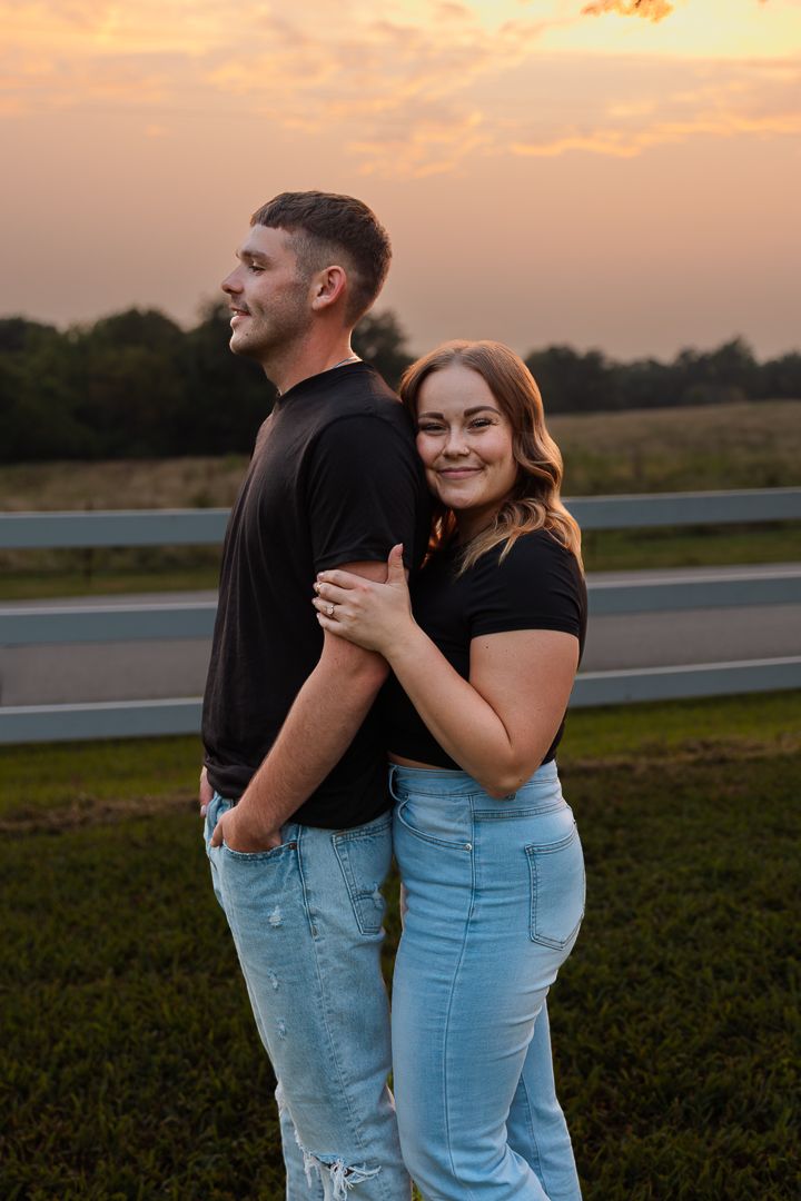 A couple shares intimate moments during a sunset photoshoot on a grassy field with warm golden lighting.