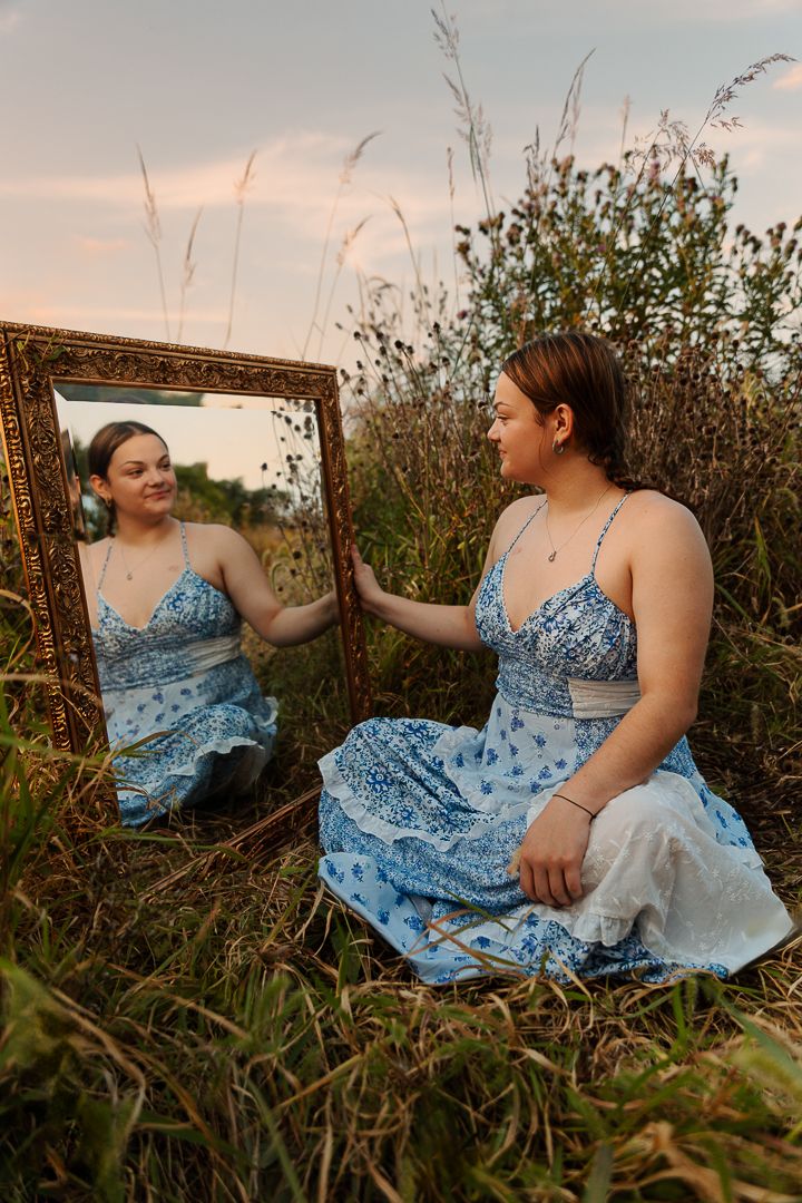 A dreamy self-reflection captured in an ornate mirror placed in a field of tall grass at sunset.
