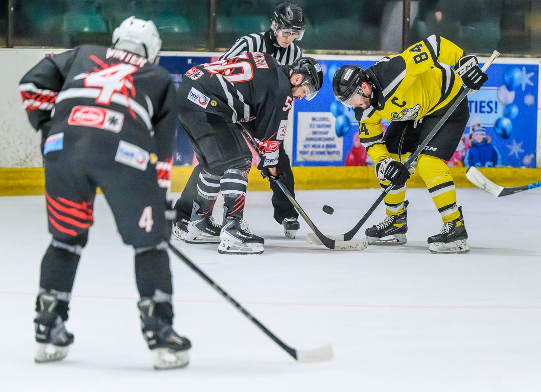 Ice hockey players battle for the puck during the opening face-off of a competitive ice hockey match.