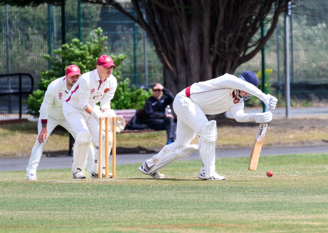 Cricket batsman stretches to defend a delivery during a competitive grassroots cricket match.