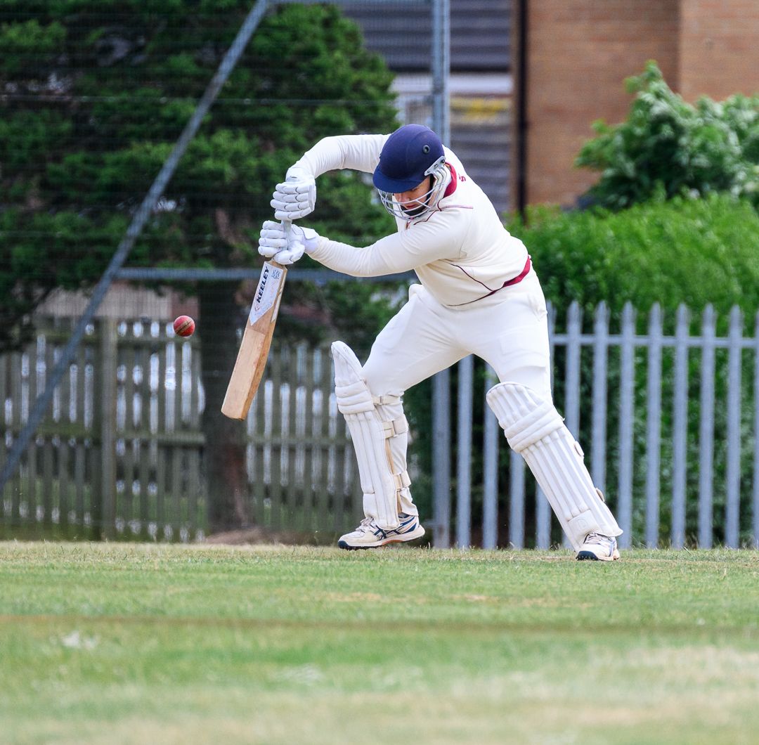 Cricket batsman stretches to defend a delivery during a competitive grassroots cricket match.